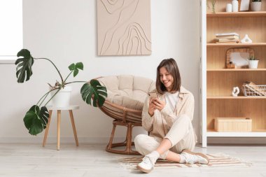 Evdeki kozanın yanında cep telefonu kullanan genç bir kadın.