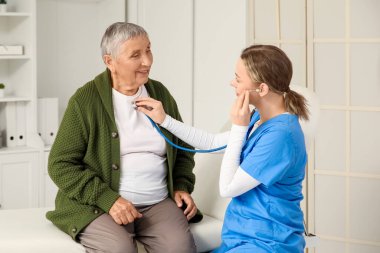 Steteskoplu hemşire klinikteki yaşlı kadını dinliyor.