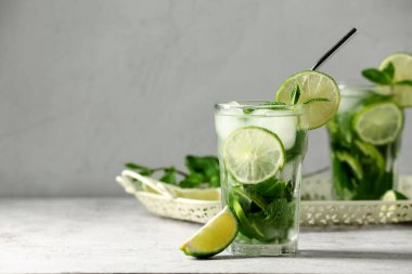 Bir bardak lezzetli mojito ve gri arka planda bir parça limon, yakın plan.