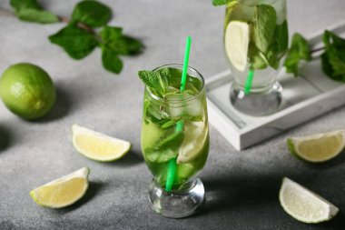 Bir bardak taze mojito ve gri arka planda bir parça limon, yakın plan.