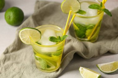 Beyaz arka planda lezzetli mojito, peçete ve limonlu kompozisyon, yakın plan.
