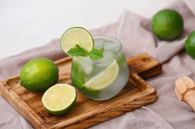 Ahşap kesim tahtası, bir bardak lezzetli mojito, beyaz arka planda peçete ve malzemeler, yakın plan.