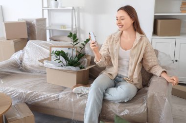 Taşınırken odada cep telefonu kullanan genç bir kadın.