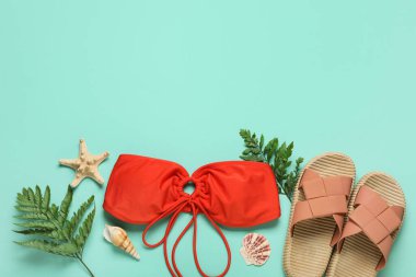 Mayolu kompozisyon, tropikal yapraklar ve turkuaz arka planda parmak arası terlikler.