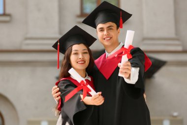 Üniversitenin yakınında, diplomalı, mutlu bir çift mezun öğrenci.