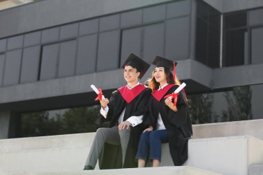 Açık havada oturan diplomalı birkaç mutlu mezun öğrenci.