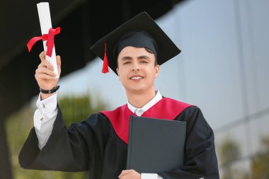 Üniversitenin yanında diploması ve kitabı olan erkek mezun.