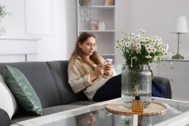 Oturma odasında cep telefonu kullanan kadına karşı vazo ve sazlık ayırıcı, yakın plan.