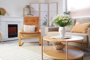 Oturma odasındaki masada, içinde papatya ve biblo olan vazo.