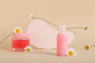 Plaster standı, şişe ve kozmetik ürünler kavanozu bej arka planda papatya çiçekleri, yakın plan