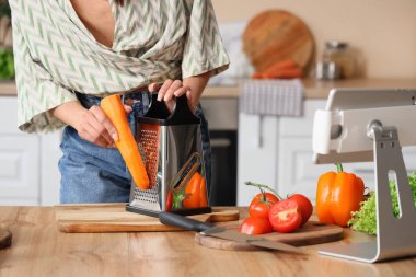 Tablet bilgisayarında yemek tarifi kitabıyla mutfakta havuç rendeleyen genç bir kadın.