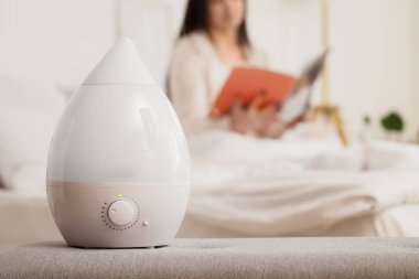 Yatak odasında dergi okuyan kadınlara karşı bankta hava nemlendirici, yakın çekim.