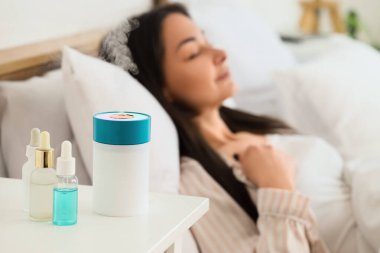 Yatak odasında uyuyan kadına karşı masasında gerekli yağları olan hava nemlendirici, yakın plan.