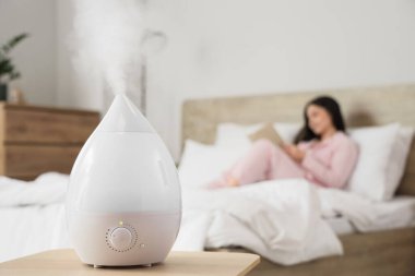 Yatak odasında kitap okuyan kadınlara karşı hava nemlendirici, yakın çekim.