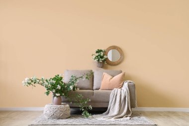 Rahat kanepe, puf ve çiçek açan yasemin çiçekleri oturma odasının iç tarafındaki bej duvarın yanında.