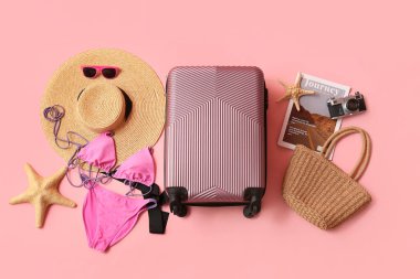 Pembe arka planda bavul, mayo ve plaj aksesuarlarıyla kompozisyon