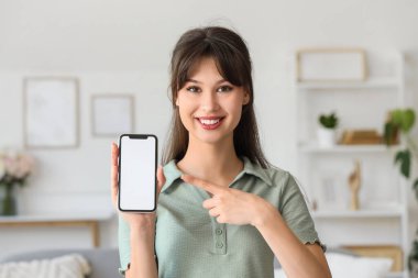 Gülümseyen genç kadın odadaki boş cep telefonuna işaret ediyor.
