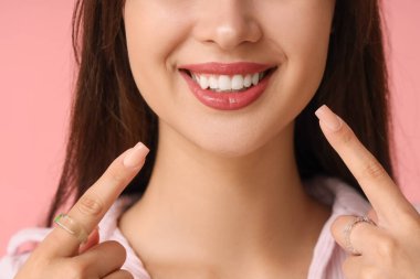 Genç bir kadın pembe arka plandaki gülüşünü işaret ediyor, yakın plan.