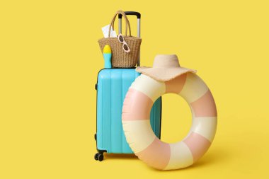 Çanta, şişirilebilir yüzük, güneş kremi şişesi ve sarı arka planda plaj aksesuarları, yakın plan.