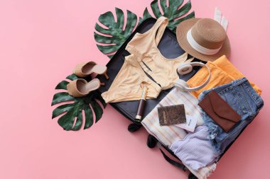 Üzerinde plaj aksesuarları ve pembe arka planda palmiye yaprakları olan valizi aç.