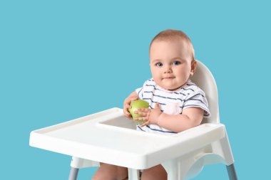 Mavi arka planda, yüksek sandalyede elmalı şirin bir bebek.