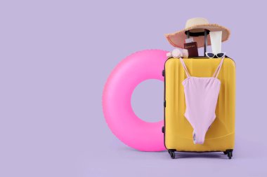 Şişirilebilir yüzük, bavul, mayo ve eflatun arka planda plaj aksesuarları.