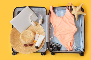 İçinde mayo, dizüstü bilgisayar, fotoğraf makinesi ve plaj aksesuarları olan bavulu aç, yakın plan.