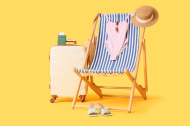 Güverte koltuğu, bavul, mayo ve sarı arka planda plaj aksesuarları, yakın plan.