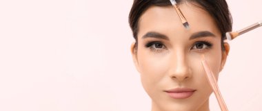 Pembe arka planda makyaj fırçası olan güzel bir genç kadın, yakın plan.