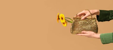 Kahverengi arkaplan üzerinde sarı Gerbera çiçekleri olan, metin için yeri olan kadın eller.