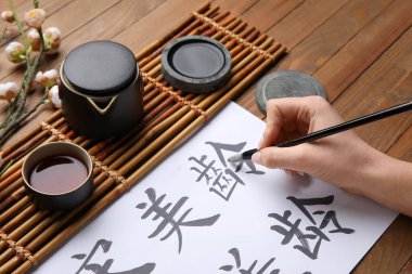 Asyalı hiyeroglifler, fırça, mürekkep ve ahşap arka planda bir fincan çay, yakın plan. Uluslararası Haiku Şiir Günü