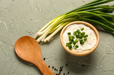 Bir kase lezzetli ekşi krema dilimlenmiş yeşil soğan ve gri arka planda biber.