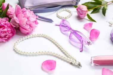 Beyaz arka planda zarif kadın aksesuarları ve güzel şakayık çiçekleri olan kompozisyon, yakın plan.