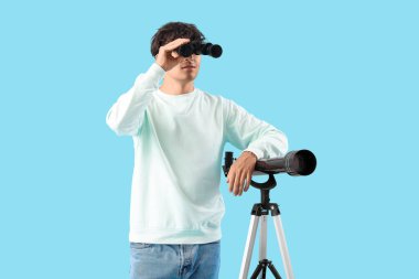 Teleskopu ve mavi arka planda dürbünü olan genç bir adam.