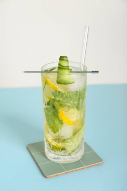 Beyaz duvarın yanındaki mavi masada limonlu, salatalıklı ve buzlu mojito.