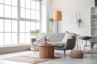 Gri kanepeli, ahşap sehpalı ve büyük pencereli aydınlık oturma odasının içi.