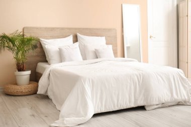 Yatak odasında beyaz yastıklı, aynalı ve çiçekli rahat bir yatak.