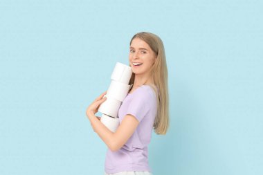 Surprised young woman with stack of toilet paper on color background
