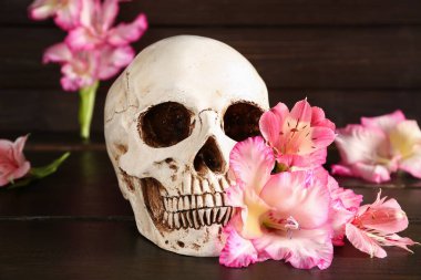Ahşap arka planda güzel zambak çiçekleri olan insan kafatası.