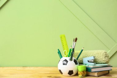 Tahta masa üzerinde farklı kırtasiye malzemesi olan futbol topu şeklinde bir tutucu.