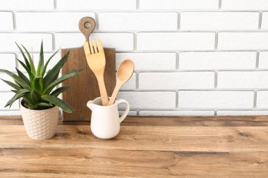 Mutfak aletleri beyaz tuğla duvarın yanındaki ahşap tezgahta.