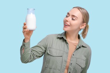 Mavi arka planda cam süt şişesi olan güzel genç bir kadın.