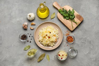 Tabak ve kavanoz lezzetli lahana turşusu ve gri arka planda farklı baharatlar.