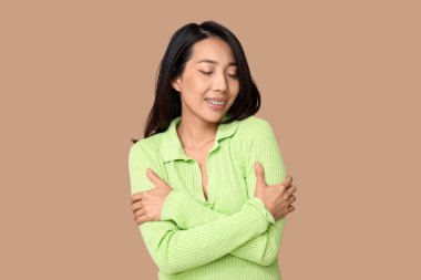 Genç Asyalı kadın kahverengi arka planda kendine sarılıyor.