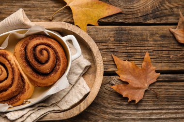 Ahşap zemin üzerinde lezzetli tarçın ruloları ve sonbahar yaprakları pişirme yemeği