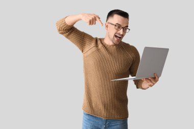 Mutlu genç adam arka planda dizüstü bilgisayarı işaret ediyor.