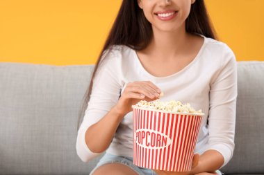 Patlamış mısırlı genç bir kadın kanepede sarı arka planda film izliyor.