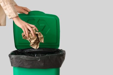 Gri duvarın yanındaki çöp kutusuna kağıt atan kadın, yakın plan.