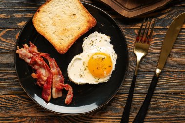 Lezzetli pastırma tabağı, kızarmış yumurta, tost ve ahşap zemin üzerinde çatal bıçak takımı.