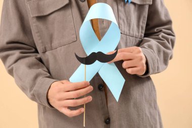 Mavi kurdeleli ve bej arka planda kağıt bıyıklı genç adam, yakın plan. Prostat kanseri farkındalığı